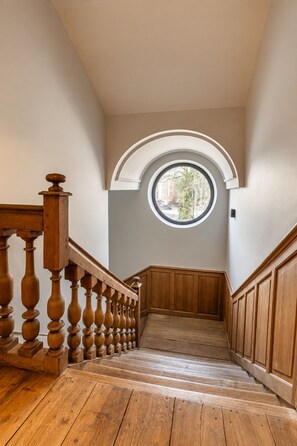Een houten trap met een balustrade die uitkomt op een plateau met een rond dakraam.