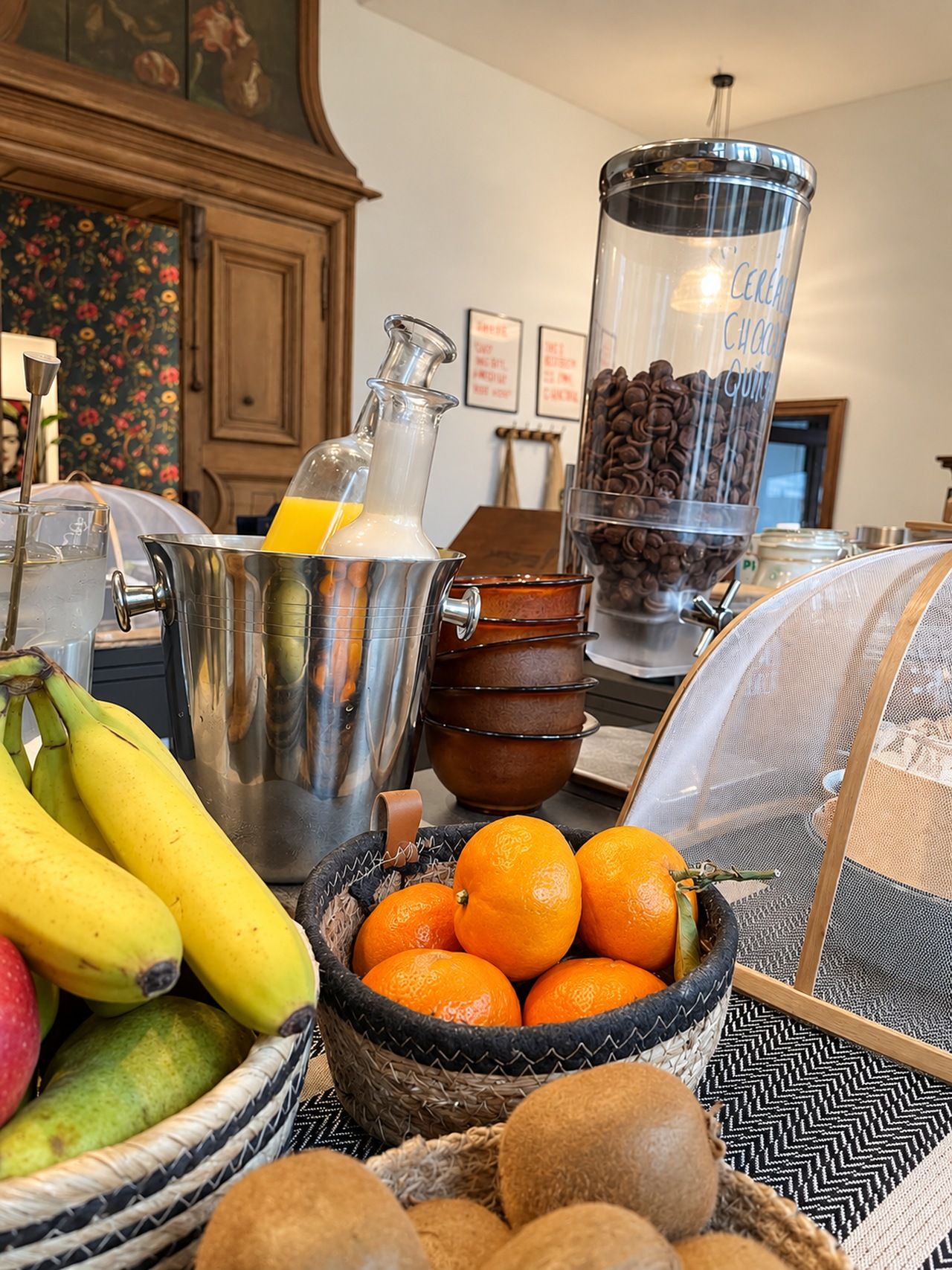 A kitchen counter with a coffee grinder, a fruit bowl with bananas and oranges, and a coffee bean dispenser.