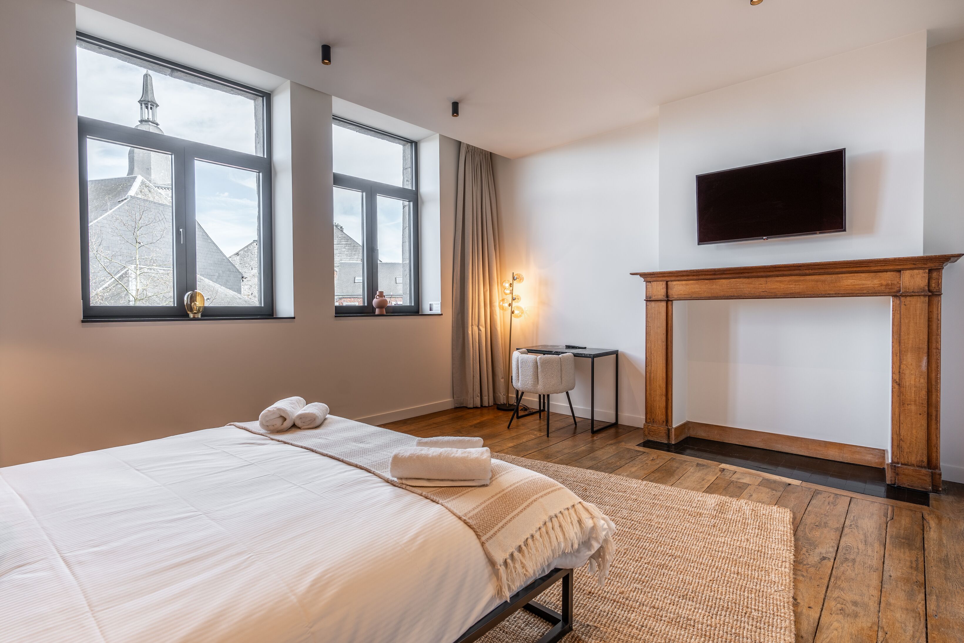 Habitación de hotel con una cama grande, chimenea, televisor y vistas a un edificio a través de las ventanas.