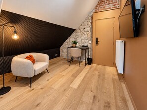 Een gezellige kamer met een schuine kap, een stenen muur, een kleine tafel met een stoel, een radiator en een vloerlamp.