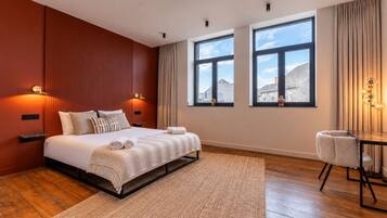 Une chambre d’hôtel moderne avec un grand lit, une petite table et deux fenêtres donnant sur la ville.