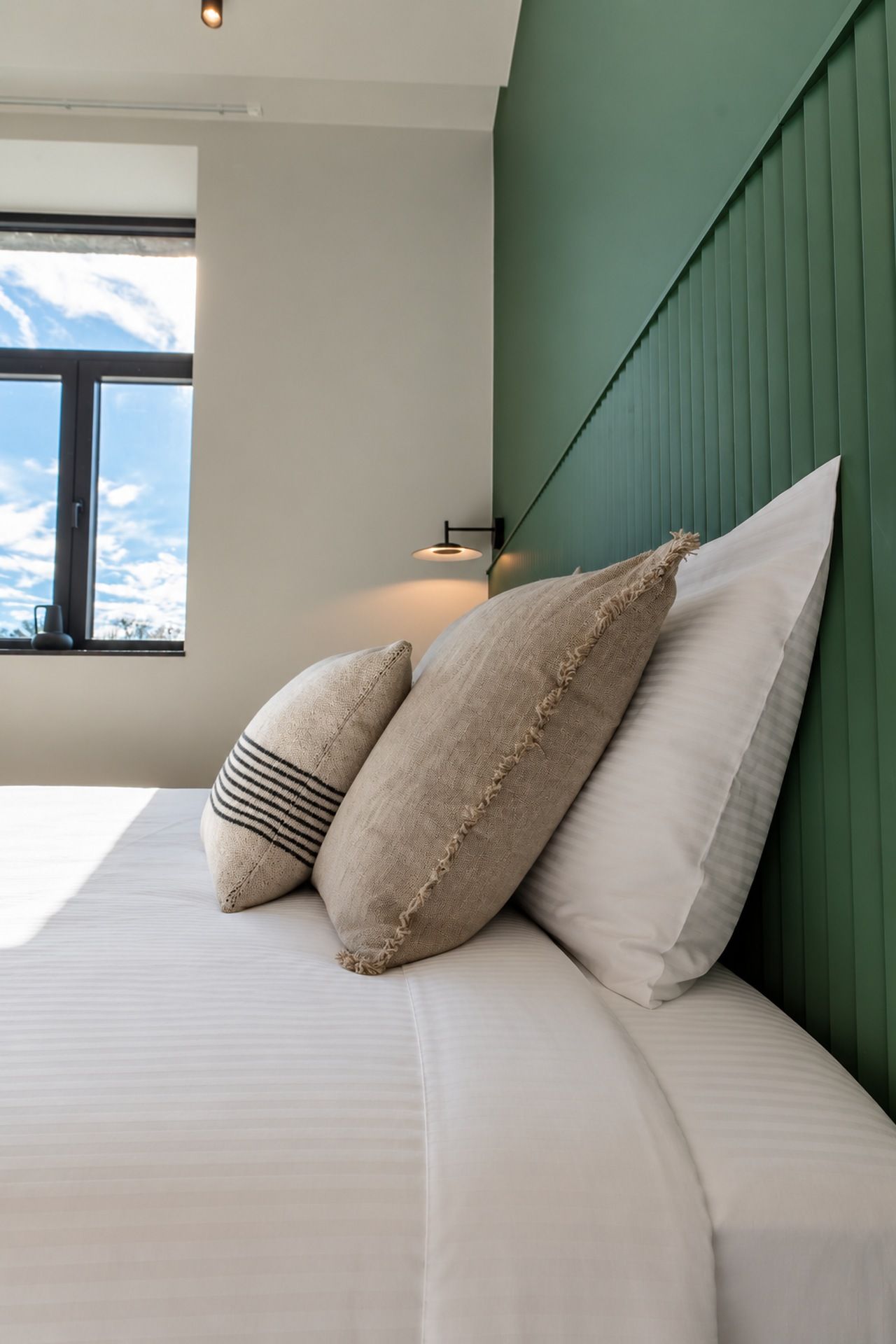 A bed with pillows and a headboard in a room with a window.