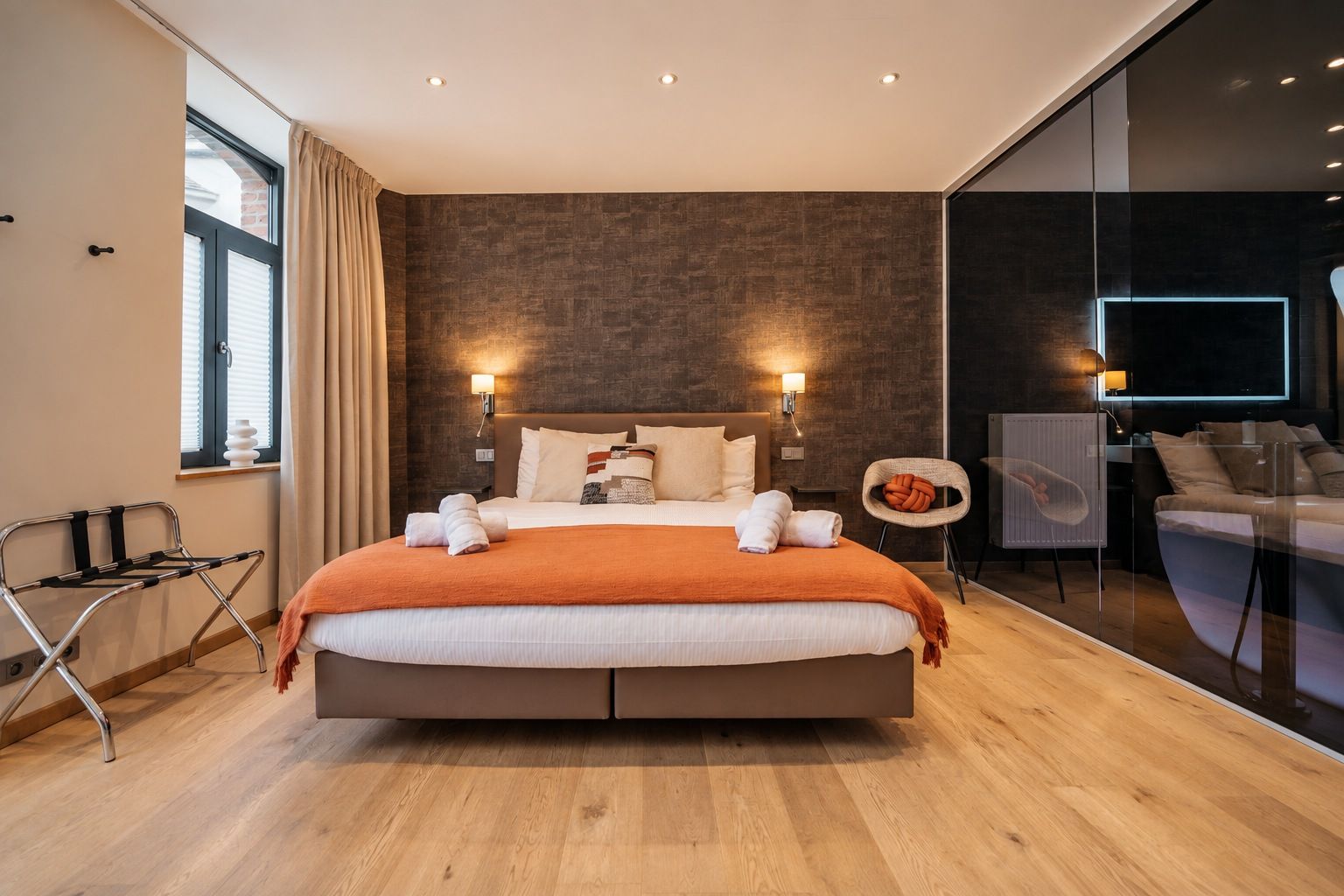 Une chambre d’hôtel moderne dotée d’un grand lit, d’une paroi en verre et d’un coin salon.