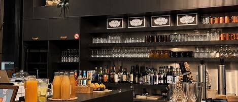 A bar area with wicker lighting fixtures, a variety of beverages, and food items on the counter.