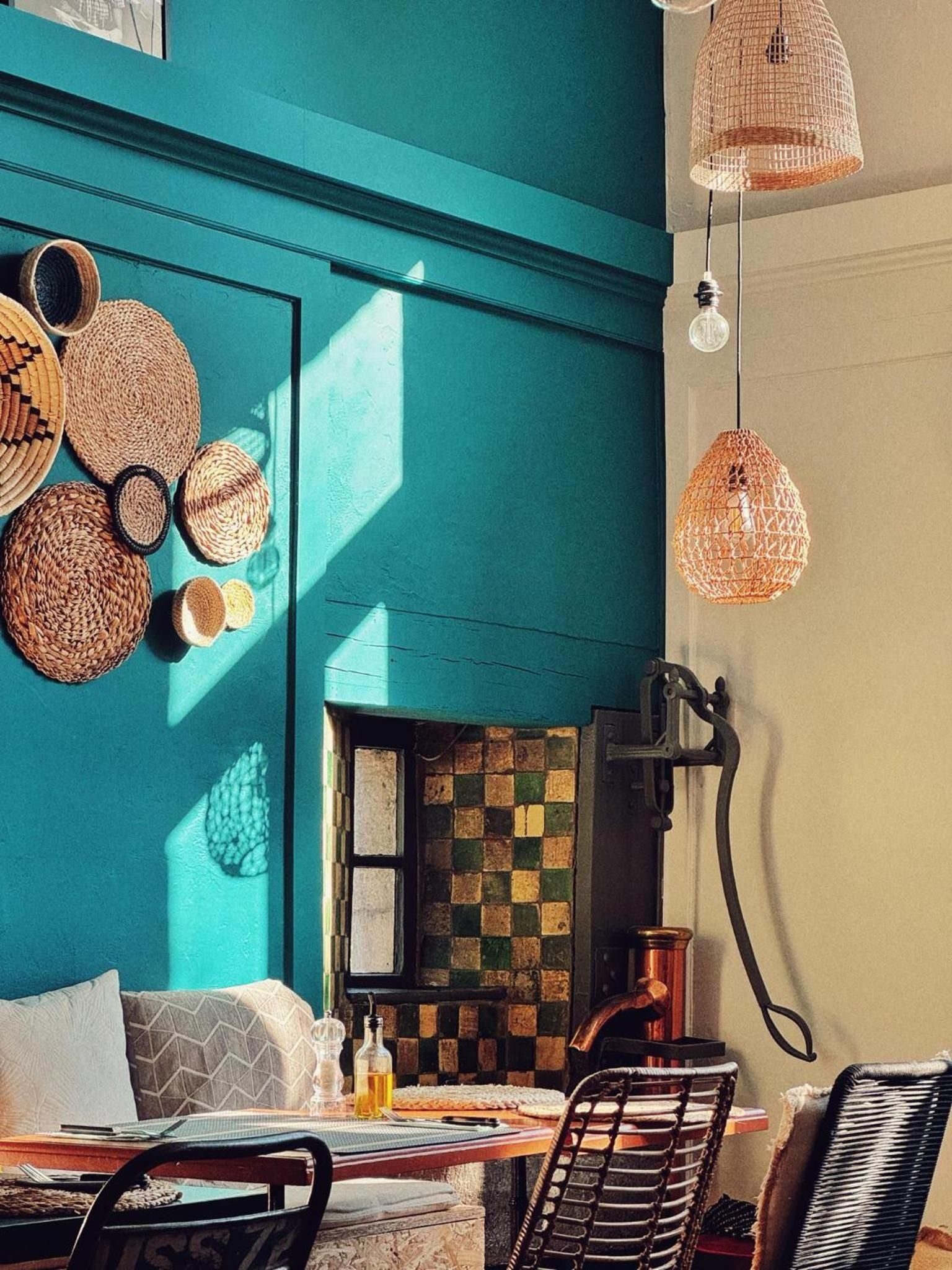A room with teal walls, a checkered tile backsplash, and a dining area with a table, chairs, and a hanging light fixture.