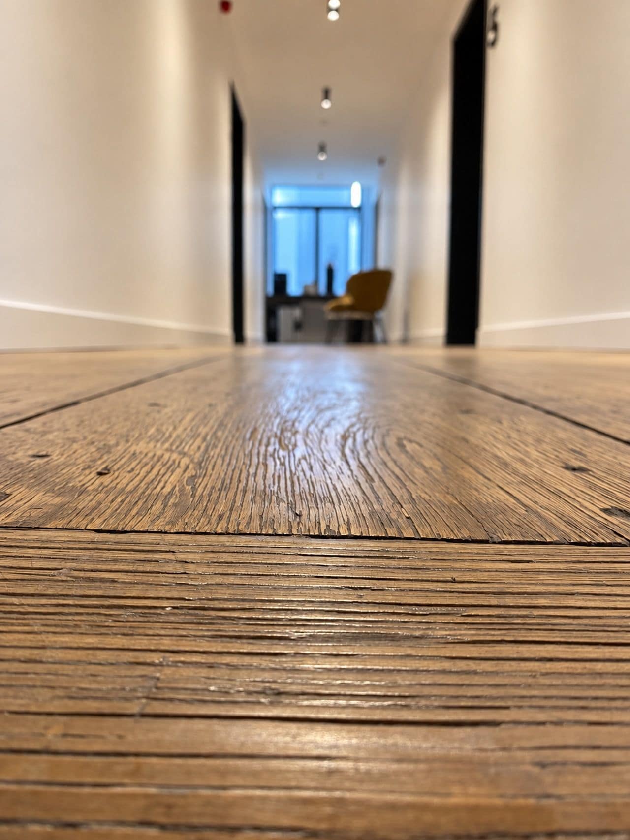 Un pavimento in legno conduce a una stanza con una finestra e una sedia.