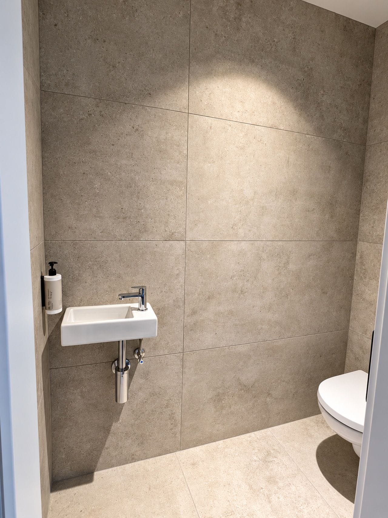 Een badkamer met een witte wastafel, toilet en beigekleurige betegelde wanden.