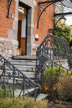 A brick building with a wooden door and a wrought iron staircase leading to the entrance. - Hôtel Le Manoir (Marche-en-Famenne)