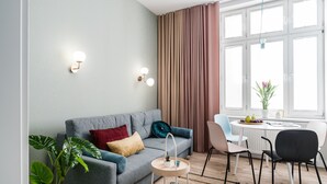 Ett modernt vardagsrum med en grå soffa, ett runt sidobord i trä och en matplats med ett vitt bord och stolar.