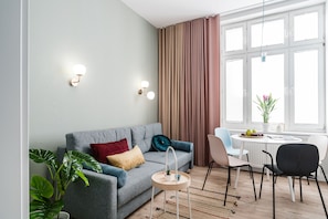 A modern living room with a grey sofa, a round wooden side table, and a dining area with a white table and chairs.