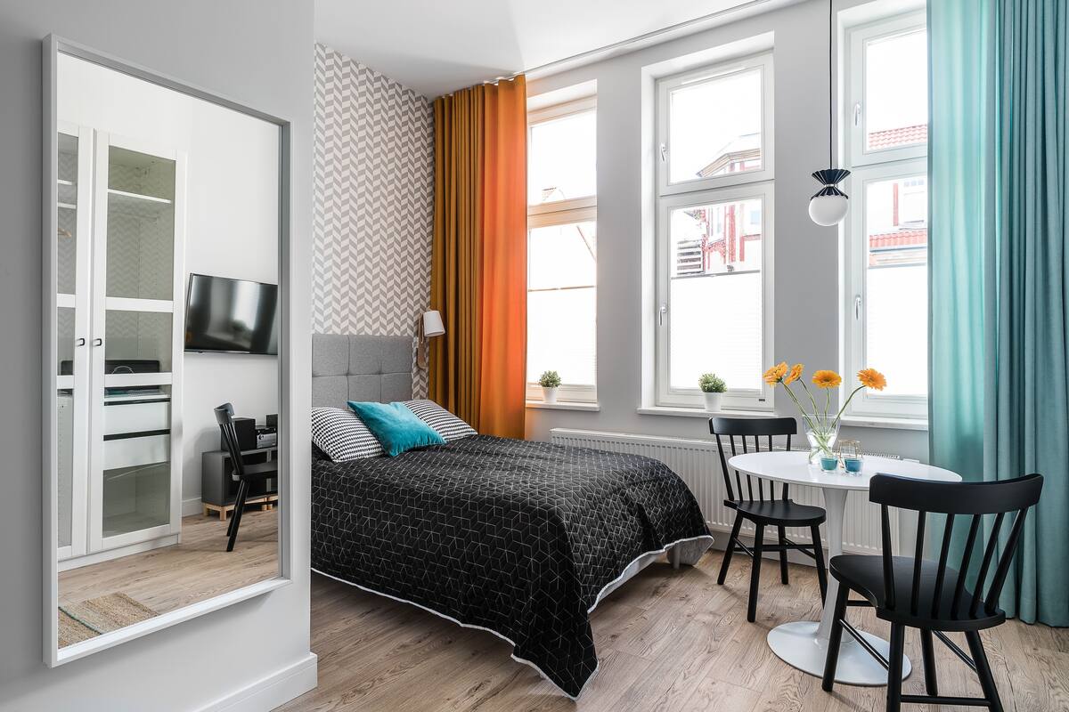 A modern bedroom with a bed, a TV, a desk with chairs, and large windows.