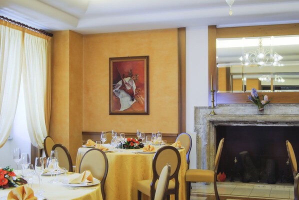 A dining area with a table set for four, a fireplace, and a painting on the wall. - Hotel Miramonti (Rieti)