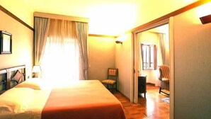 Una habitación de hotel con una cama, una silla, un escritorio y una puerta que da a otra habitación.
