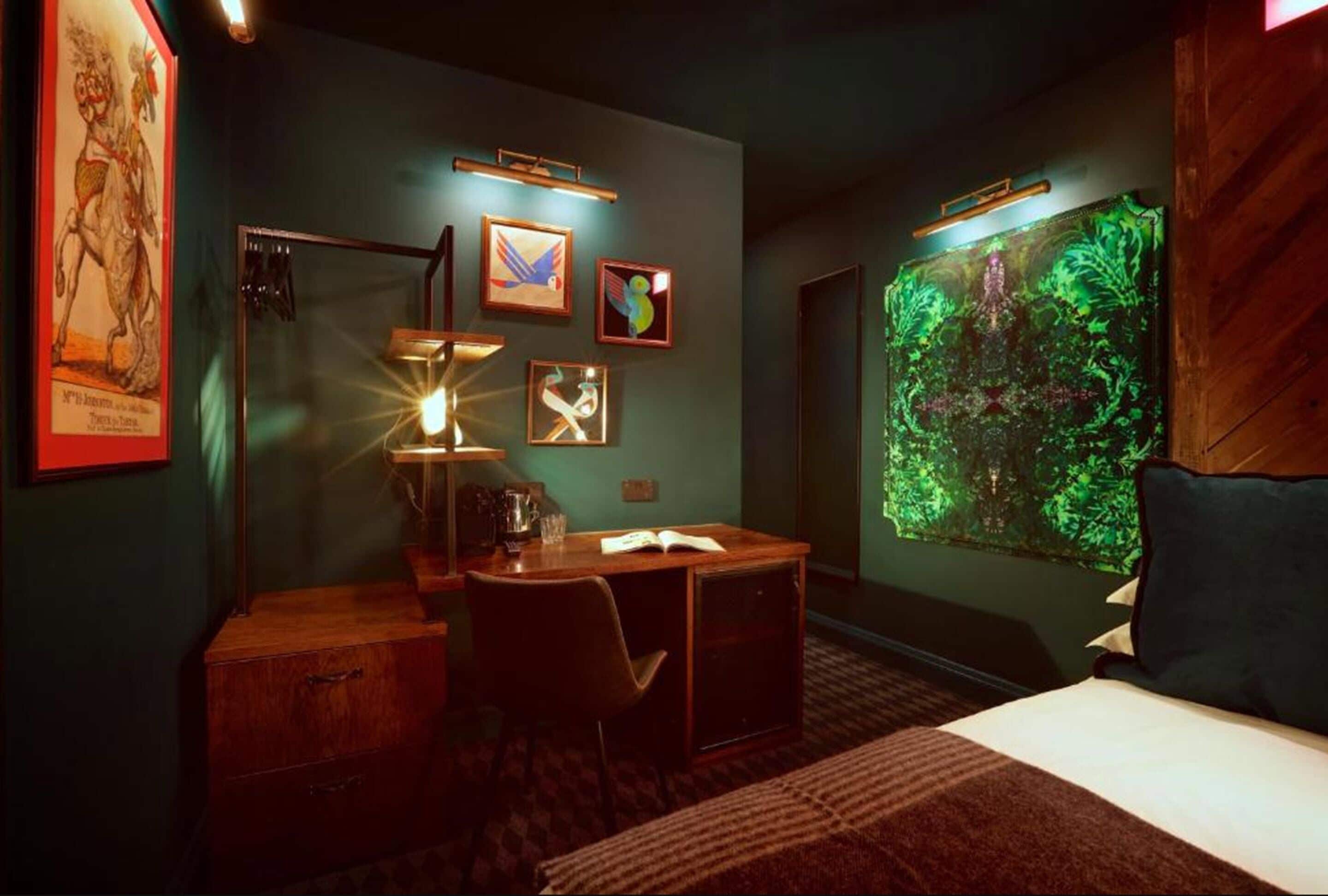 Ein Hotelzimmer mit Schreibtisch, Bett, großem Fenster mit Blick auf Bäume und Kunstwerken an den Wänden.