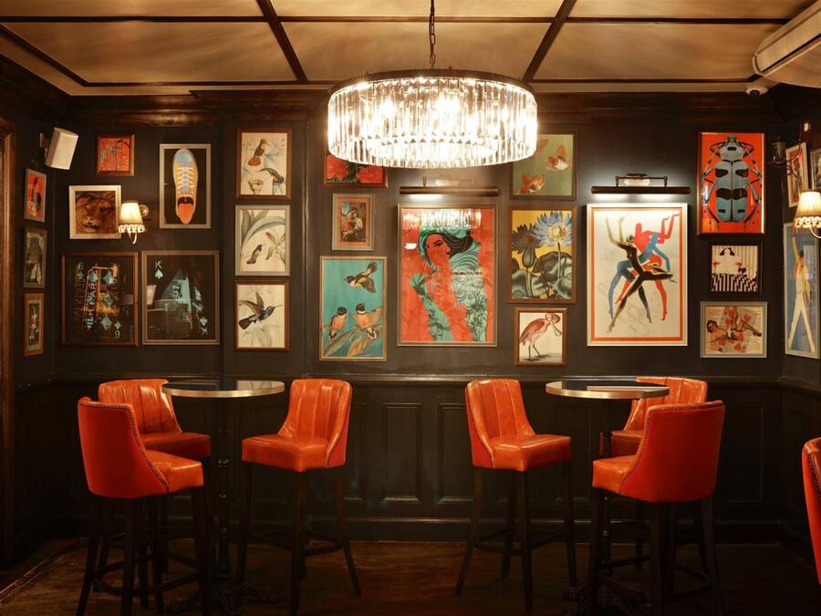 Una zona de bar con taburetes de cuero rojo, un candelabro y varias obras de arte enmarcadas en las paredes.