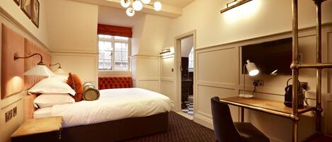 A hotel room with a bed, a desk, a chair, a TV, and a bathroom visible through an open door.