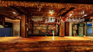 A rustic bar area with wooden beams, shelves of liquor bottles, and hanging glassware. - Hotel Dumanov (Bansko)