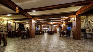 A spacious hall with wooden beams, stone walls, and tiled flooring. Tables and chairs are arranged for dining. - Hotel Dumanov (Bansko)
