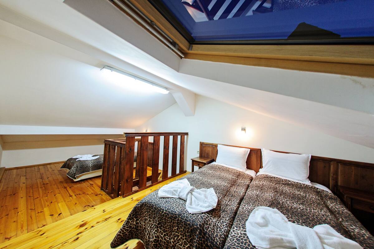 A bedroom with a sloped ceiling, a skylight, a bed with a leopard print bedspread, wooden flooring, and a wooden bench.