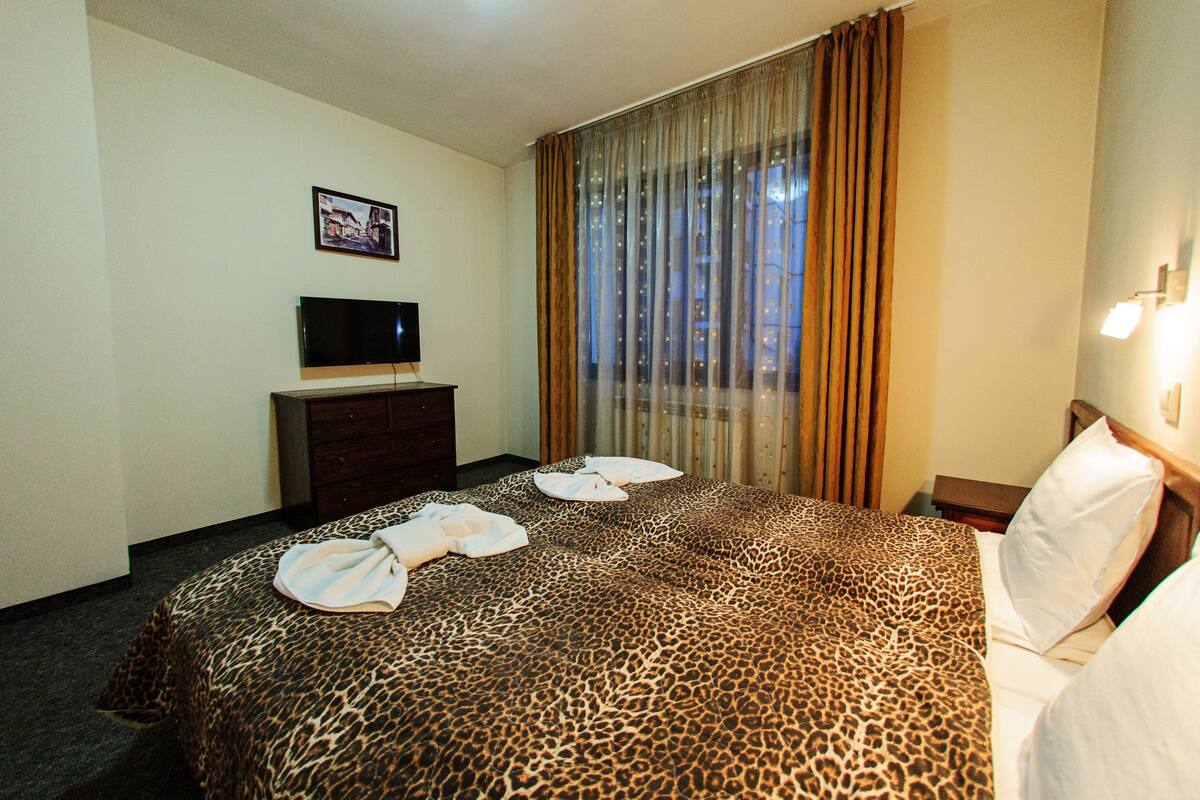 A hotel room with a bed, a television on a dresser, and a window with curtains.