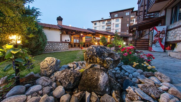 A hotel courtyard with a stone wall, large rocks, and flowers. - Hotel Dumanov (Bansko)