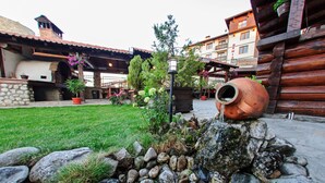A courtyard with a rustic stone wall, a large terracotta pot, and potted plants. - Hotel Dumanov (Bansko)