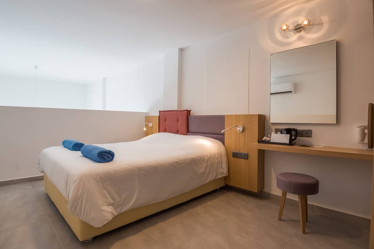 Una habitación de hotel moderna con una cama, un escritorio, una silla, un espejo y un taburete pequeño.