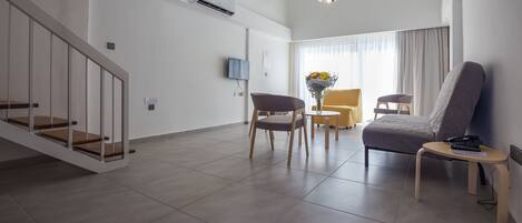 A modern living room with a staircase, a flat-screen TV, a dining table with chairs, and a sofa.