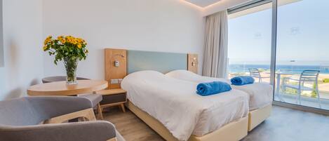A modern hotel room with a large bed, a small desk, a chair, and a view of the sea.