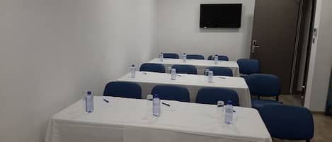 Un salón de conferencias con mesas, sillas, botellas de agua y un televisor de pantalla plana en la pared.