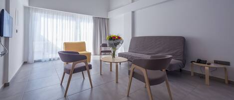 Una sala de estar moderna con un sofá gris, dos sillones, una mesita redonda con un jarrón de flores y un televisor en la pared.