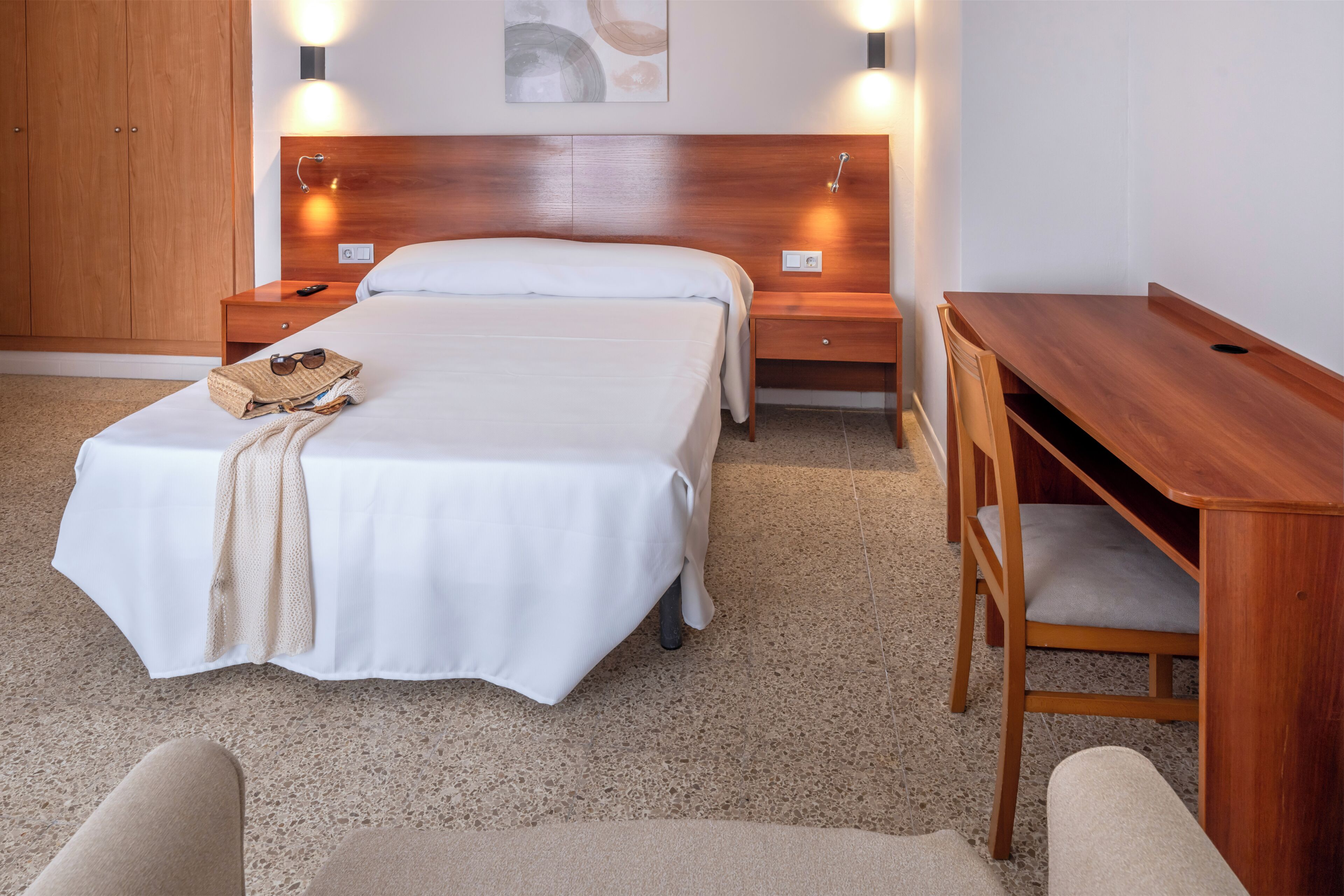 A hotel room with a bed, bedside tables, a desk, and a chair.