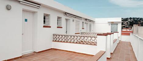 Un edificio blanco con un patio adoquinado, una puerta con el número 403 y una vista de un paisaje urbano al fondo.