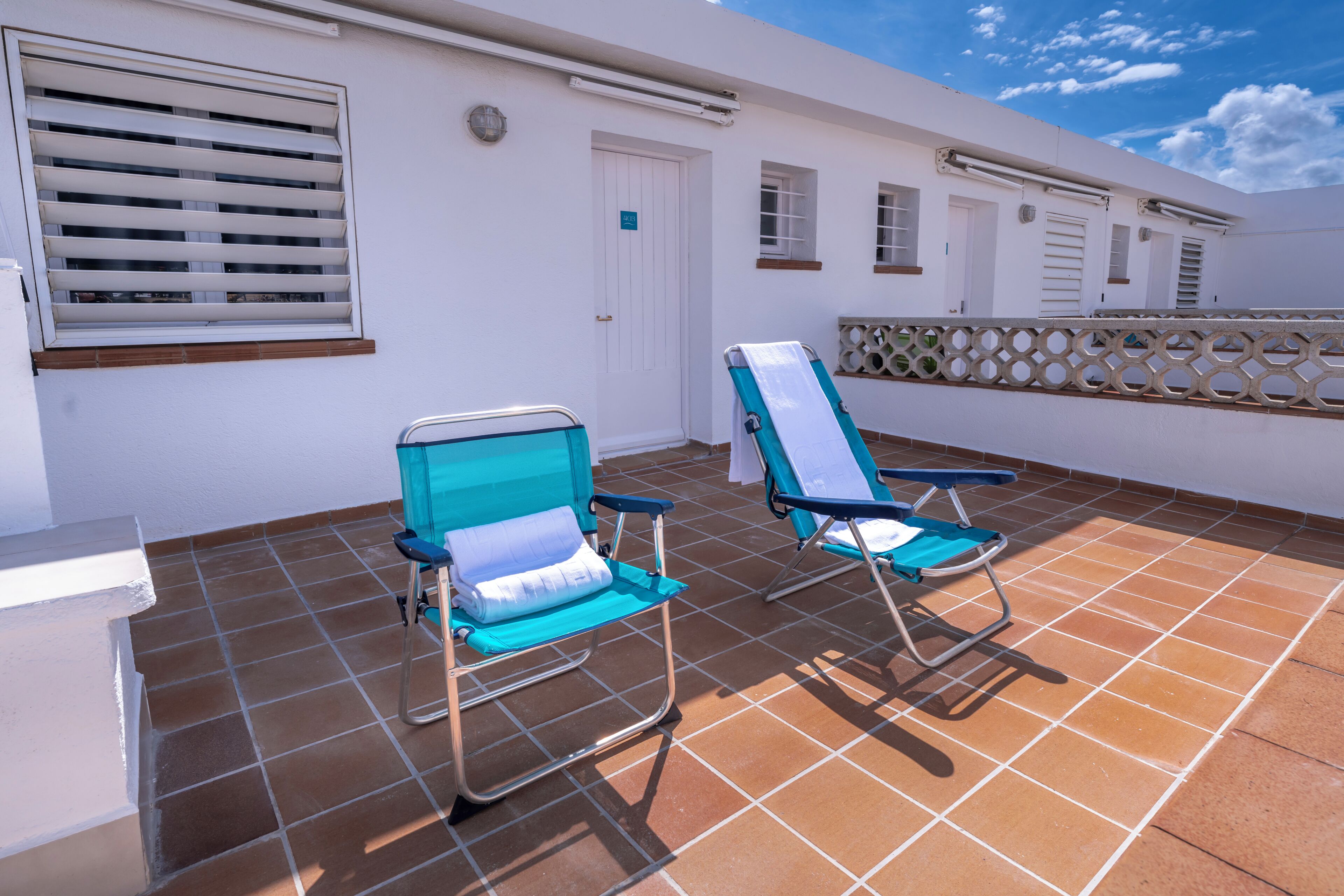 Un balcon avec deux fauteuils bleus, une porte blanche et une fenêtre avec des stores.