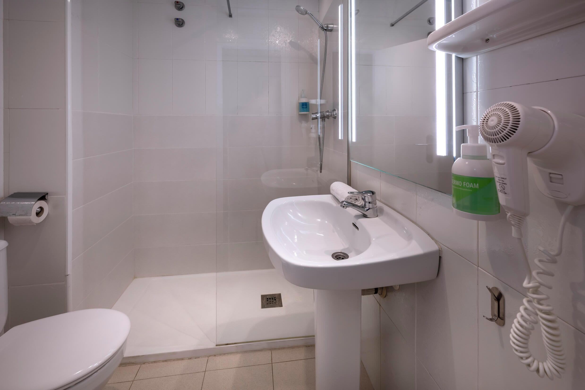 Un baño con inodoro, lavabo, ducha y secador de pelo.