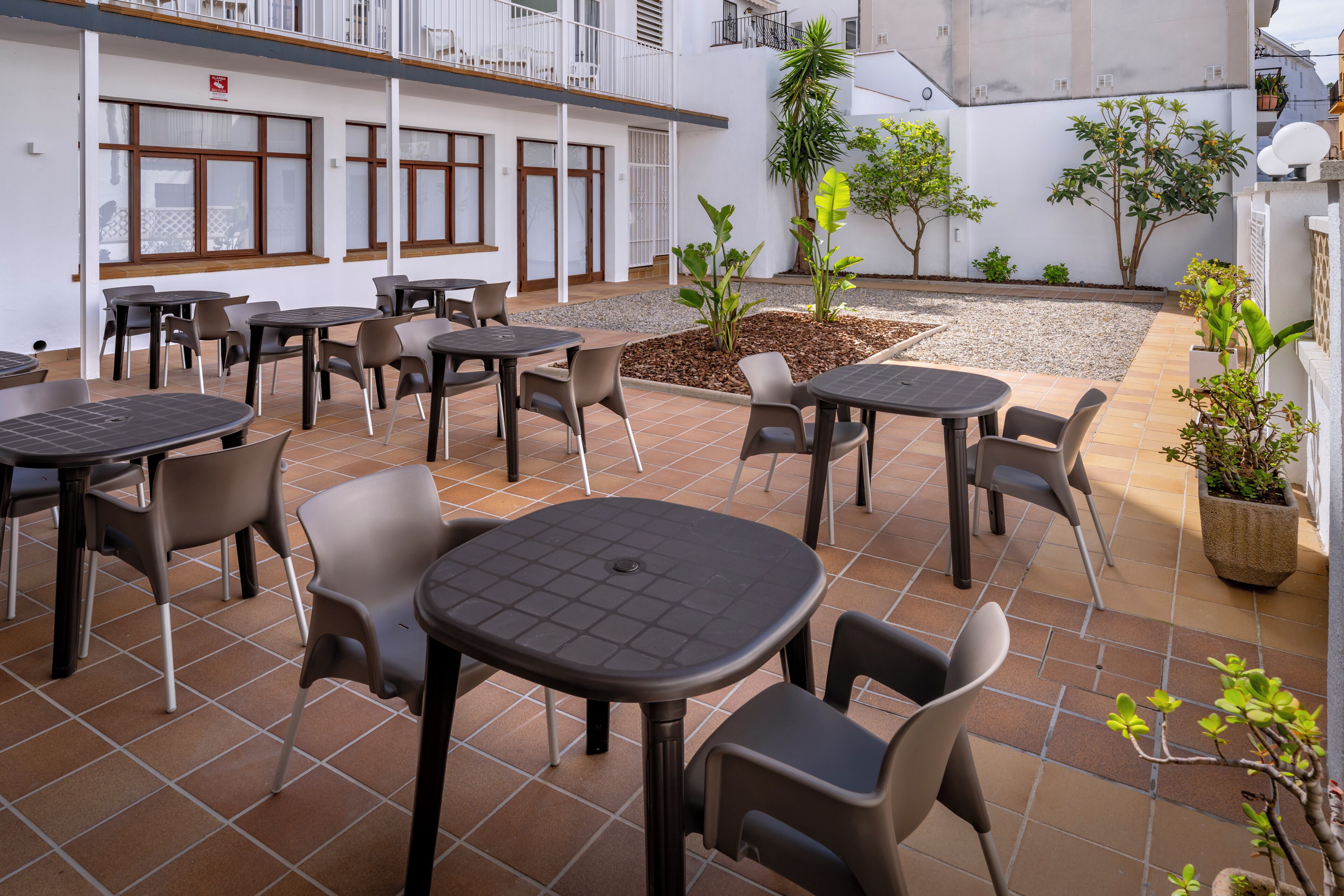 An outdoor patio area with multiple tables and chairs, surrounded by white walls and potted plants.