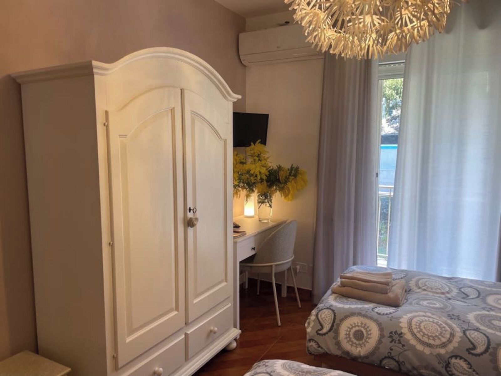 A bedroom with a bed, a wardrobe, a desk with a chair, and a window with curtains.
