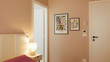 A hotel room with a bed, a bedside lamp, a door, and two framed artworks on the wall.