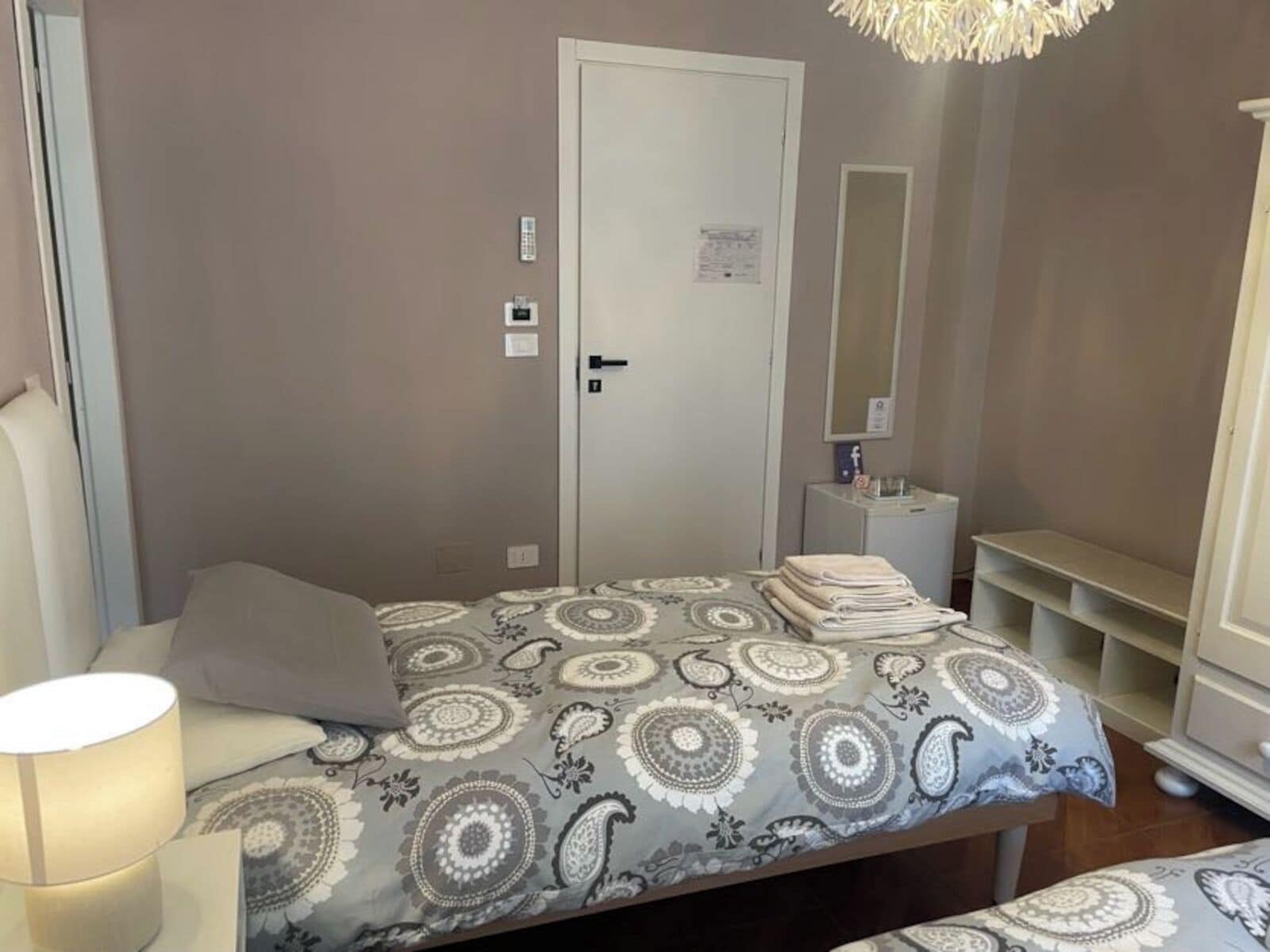 A bedroom with a bed, a bedside table, a lamp, a wardrobe, and a door with a lock.