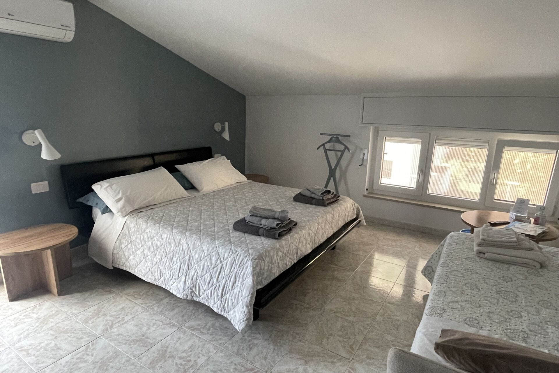 A bedroom with a bed, a bedside table, a lamp, a window, and a chair.