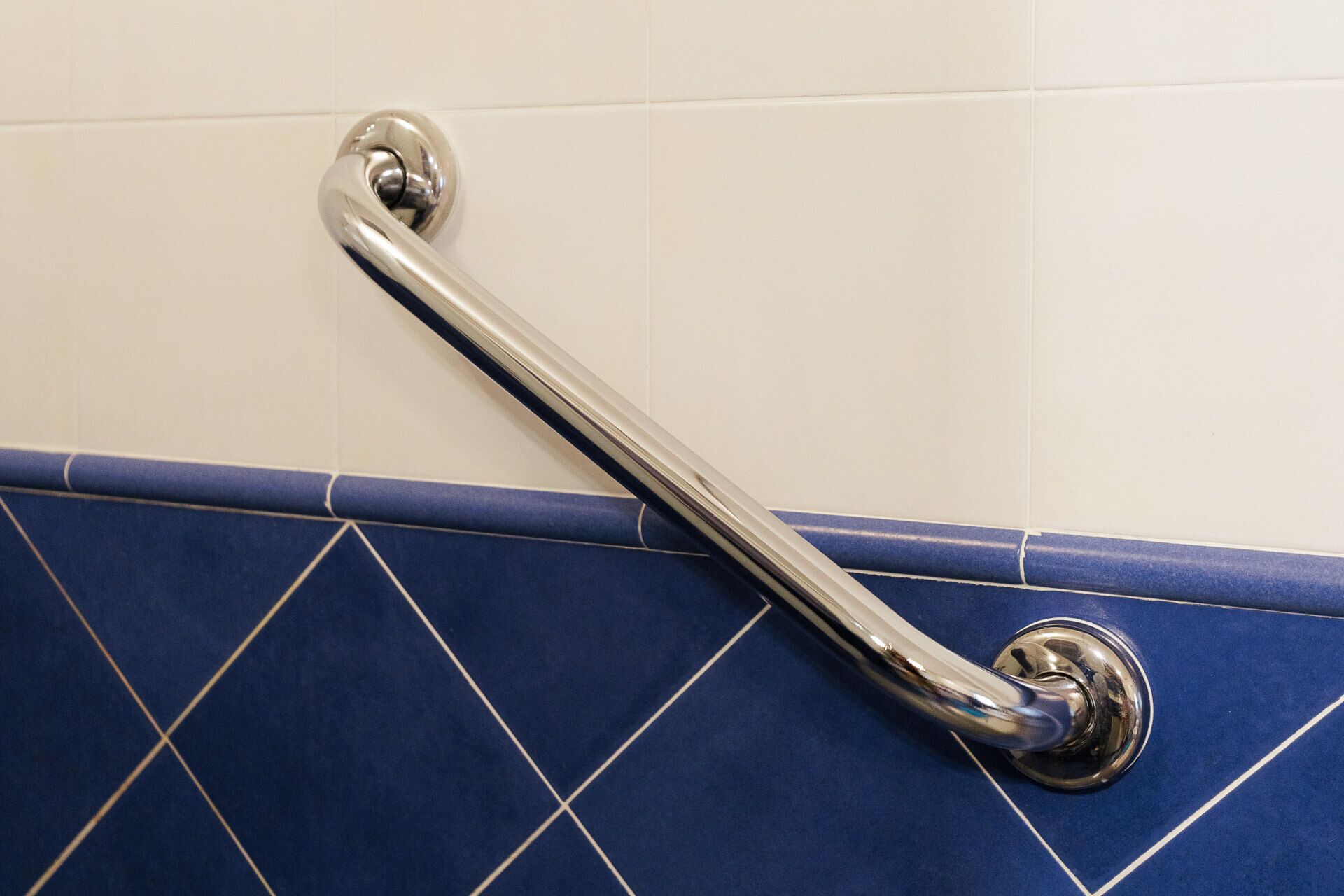 A bathroom with a blue tiled floor and a chrome grab bar mounted on the wall.