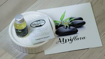 Una bottiglia di crema viso nutriente Alpiflora, un contenitore di ceramica bianca e un depliant a tema spa.