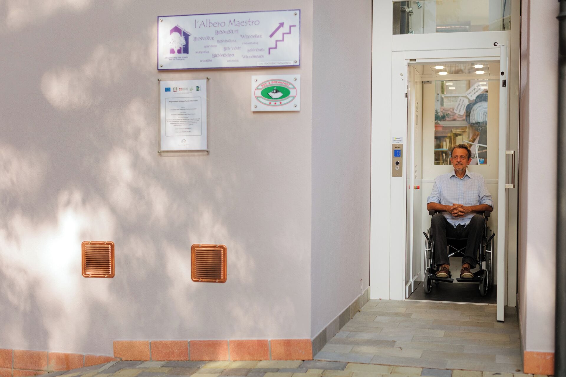 A man in a wheelchair entering a building with a sign reading "Welcome" and a green sign indicating a restaurant.