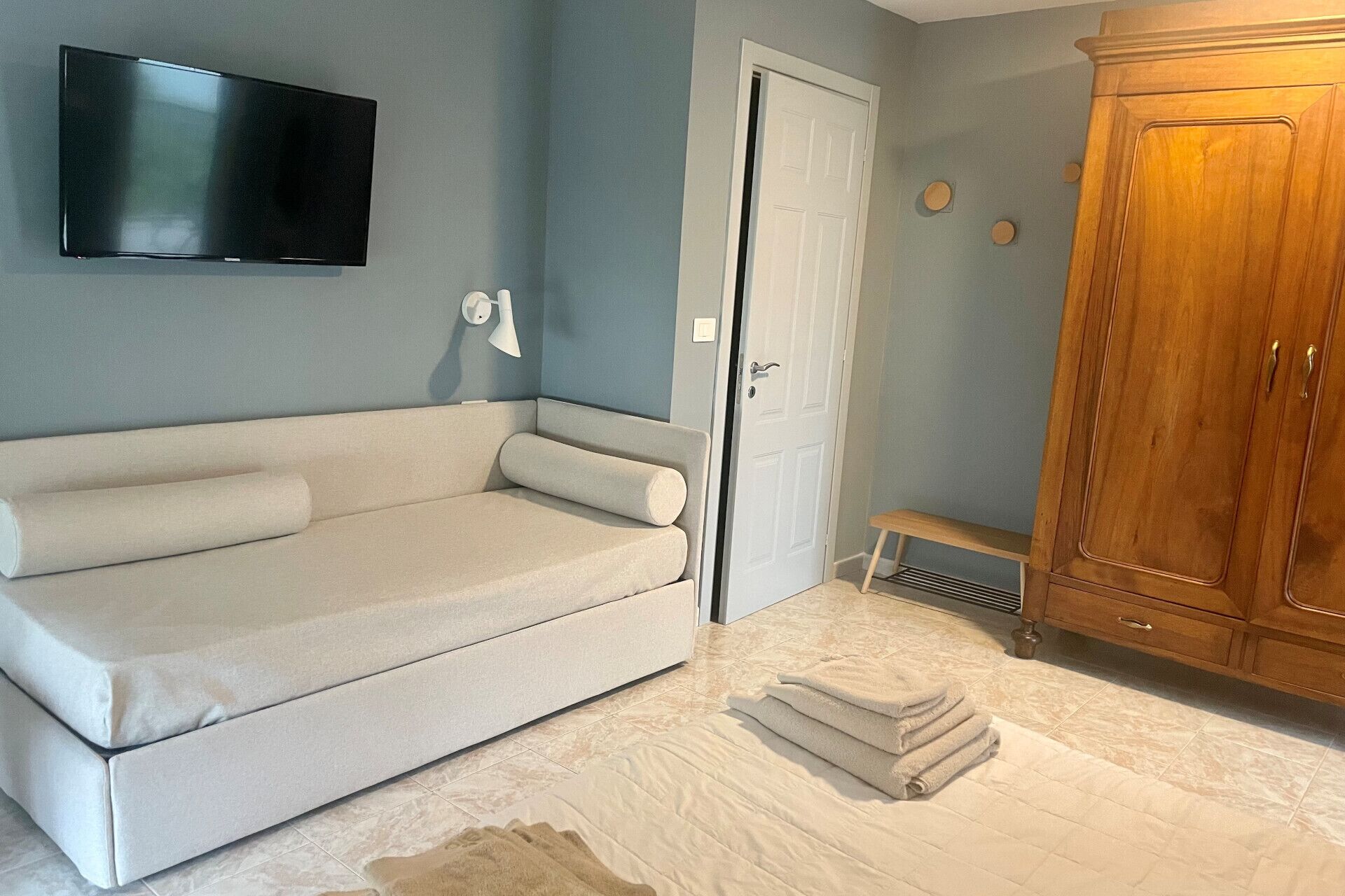 Una habitación con sofá beige, televisión en la pared, armario de madera y una puerta.