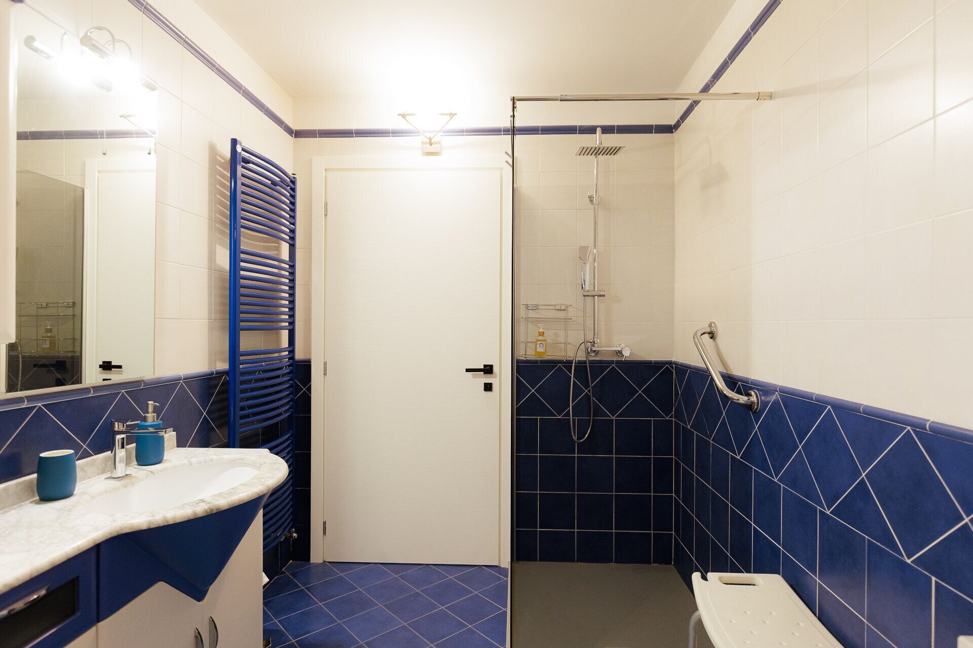 Un baño con una puerta blanca, una zona de ducha con azulejos azules y un lavabo con encimera azul.