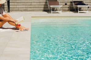 A poolside area with a person reading a book, a glass of red wine, and a plate of blueberries. - B&B L'Albero Maestro (Borgofranco d'Ivrea)