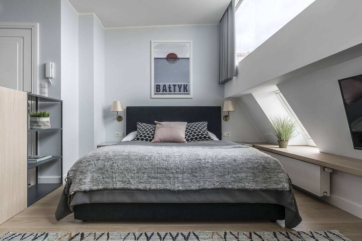 Un dormitorio moderno con una cama grande, un tragaluz, un televisor montado y una obra enmarcada en la pared.