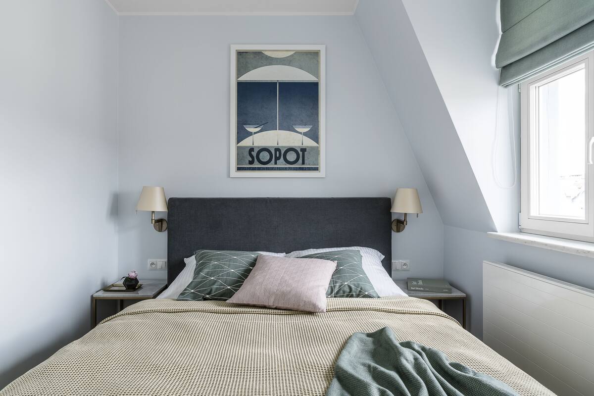 Un dormitorio con cama, dos mesitas de noche, una lámpara, ventana con vistas y un cartel en la pared.