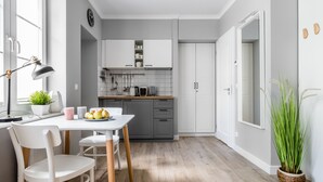 A modern kitchen with white cabinetry, a dining table with chairs, a potted plant, and a clock on the wall. - Sanhaus Apartments - Parkowa (Sopot)