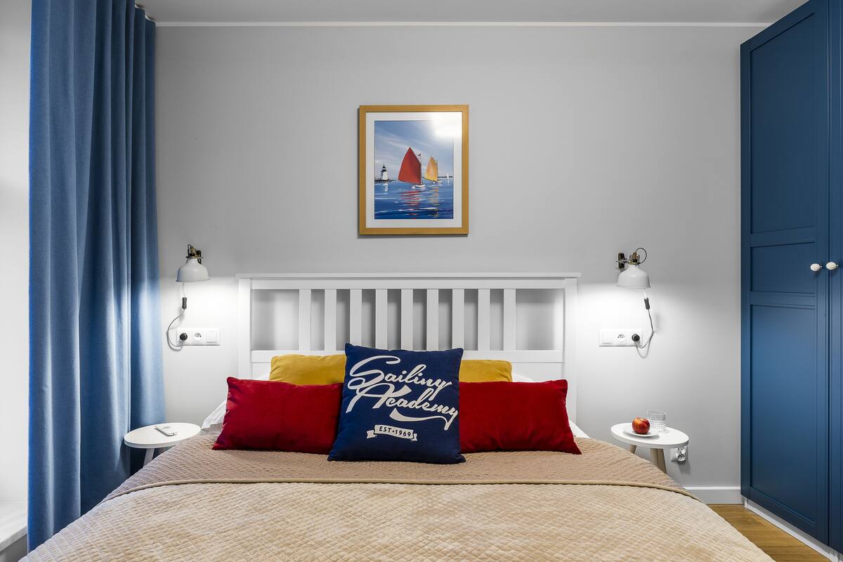Habitación de hotel con cama, mesita de noche, una pequeña mesa, un cuadro enmarcado en la pared y una puerta azul.